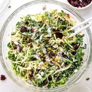 Sweet kale salad with pepitas and cranberries and poppy seed dressing in glass bowl.