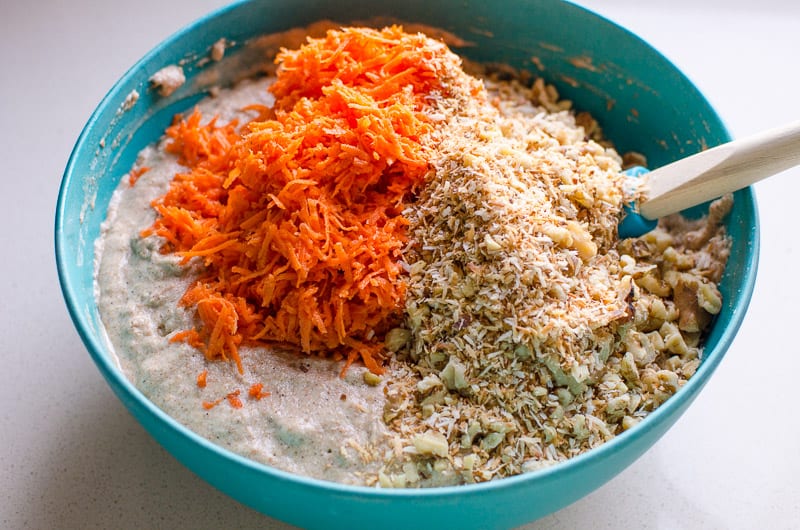 Healthy carrot cake batter with shredded carrots and toasted nuts and coconut flakes in blue bowl. 