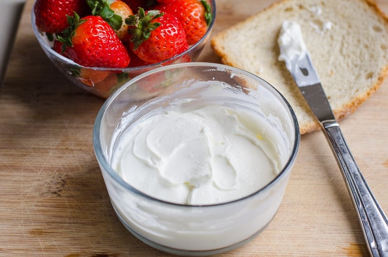 glass bowl with cream cheese, knife and strawberries on a cutting board