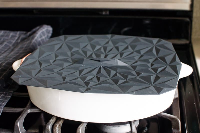 White baking dish covered with black silicone lid on a stovetop.