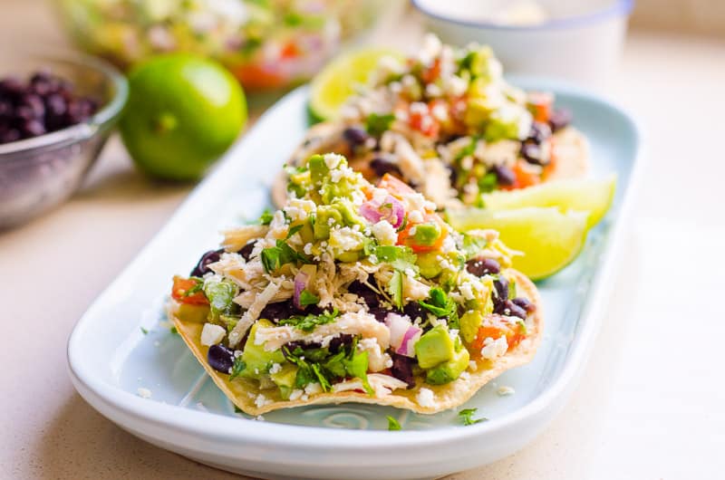 Chicken tostadas with avocado, black beans, tomato, red onion and garnished with cilantro on a serving dish