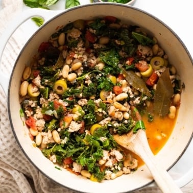 Ground Turkey Stew with kale, beans and olives in white pot.