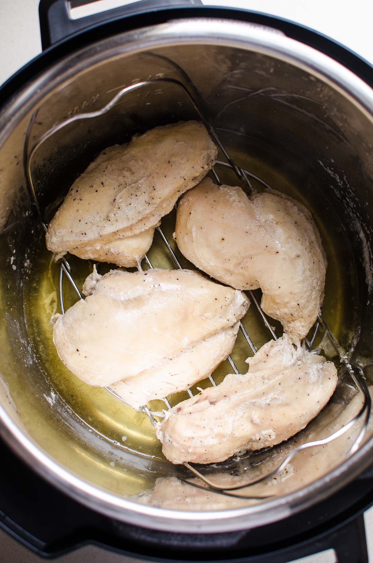 Instant Pot chicken breast on a trivet inside the pot and broth at the bottom.