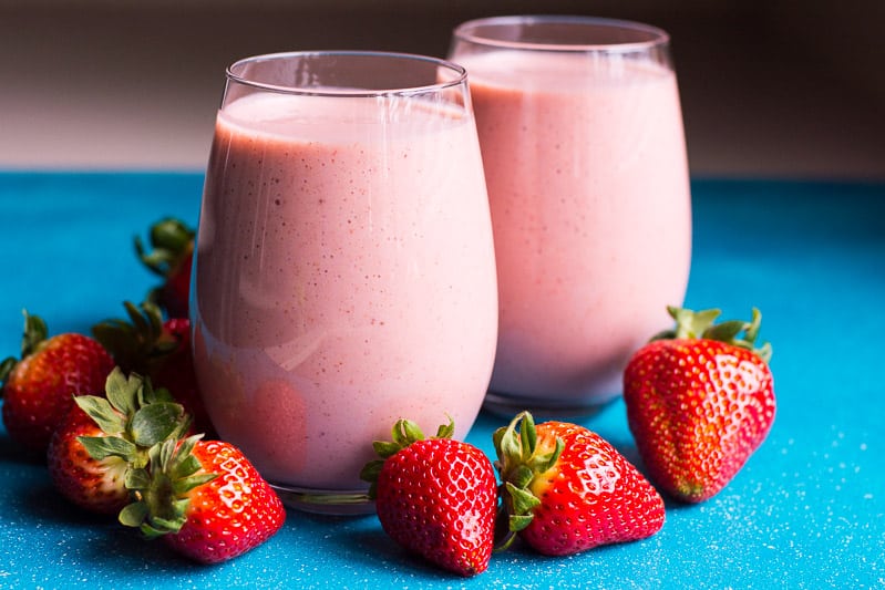 two glasses with strawberry smoothie and fresh berries nearby