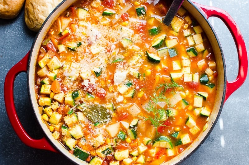 Vegetable soup with zucchini, corn, tomatoes, parmesan cheese and dill in red pot.