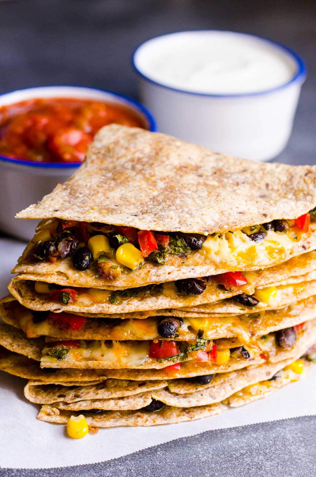 A stack of veggie quesadillas with small bowls of salsa and Greek yogurt behind.