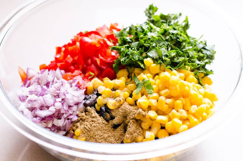 Corn, bell peppers, cilantro, red onion, black beans and cumin in glass bowl. 