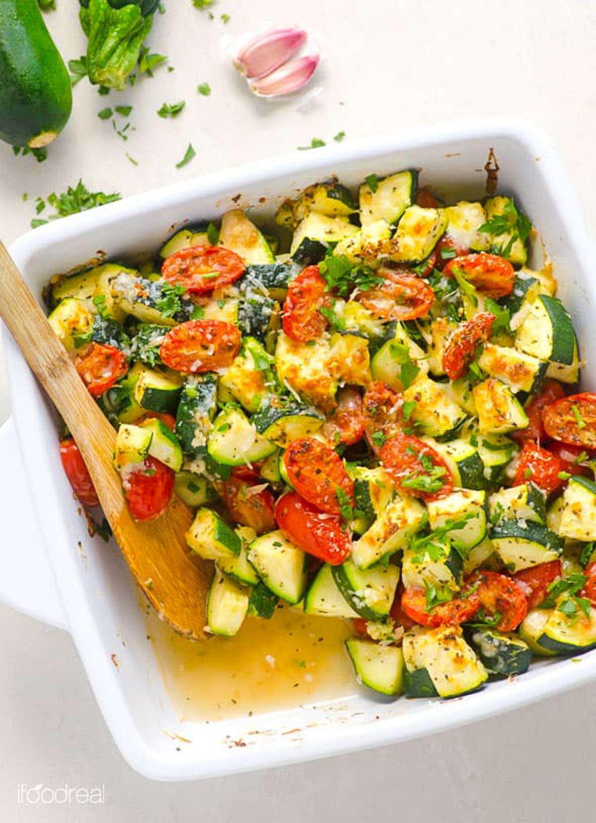 Healthy zucchini tomato bake in a casserole dish with a wooden spoon.