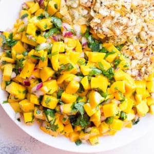 Mango salsa served with chips in white bowl.