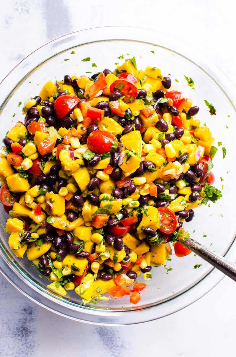Mango black bean salad in glass bowl with a spoon.