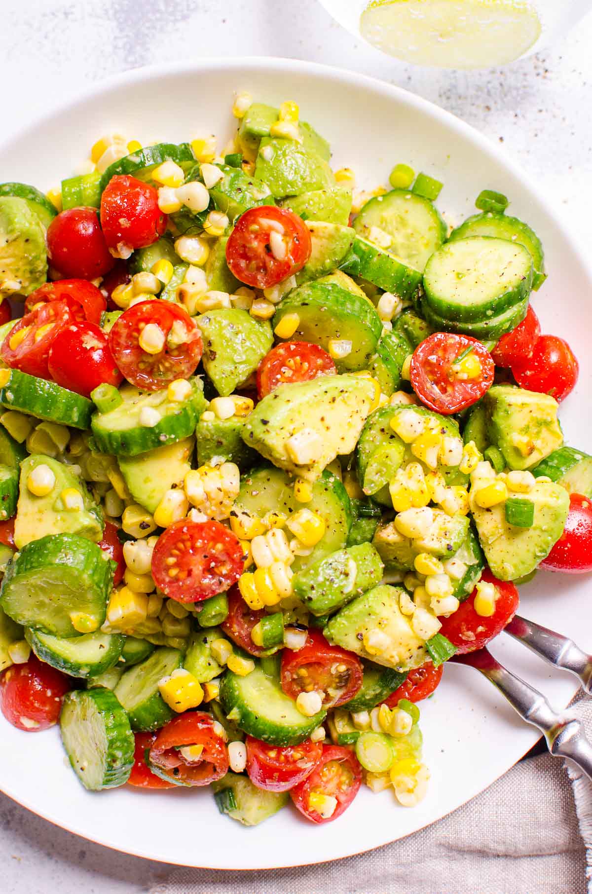 Avocado corn salad on white plate with spoon and fork.