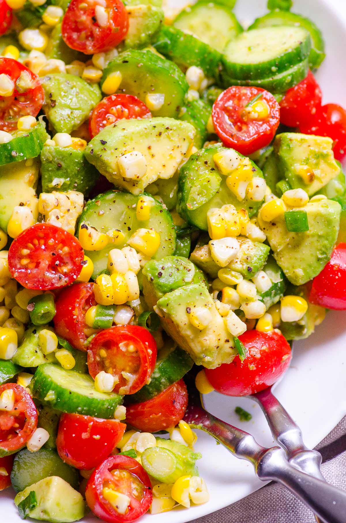 Closeup of avocado corn salad garnished with green onions and black pepper.