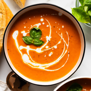 Creamy tomato soup served in bowls and garnished with coconut milk and fresh basil.