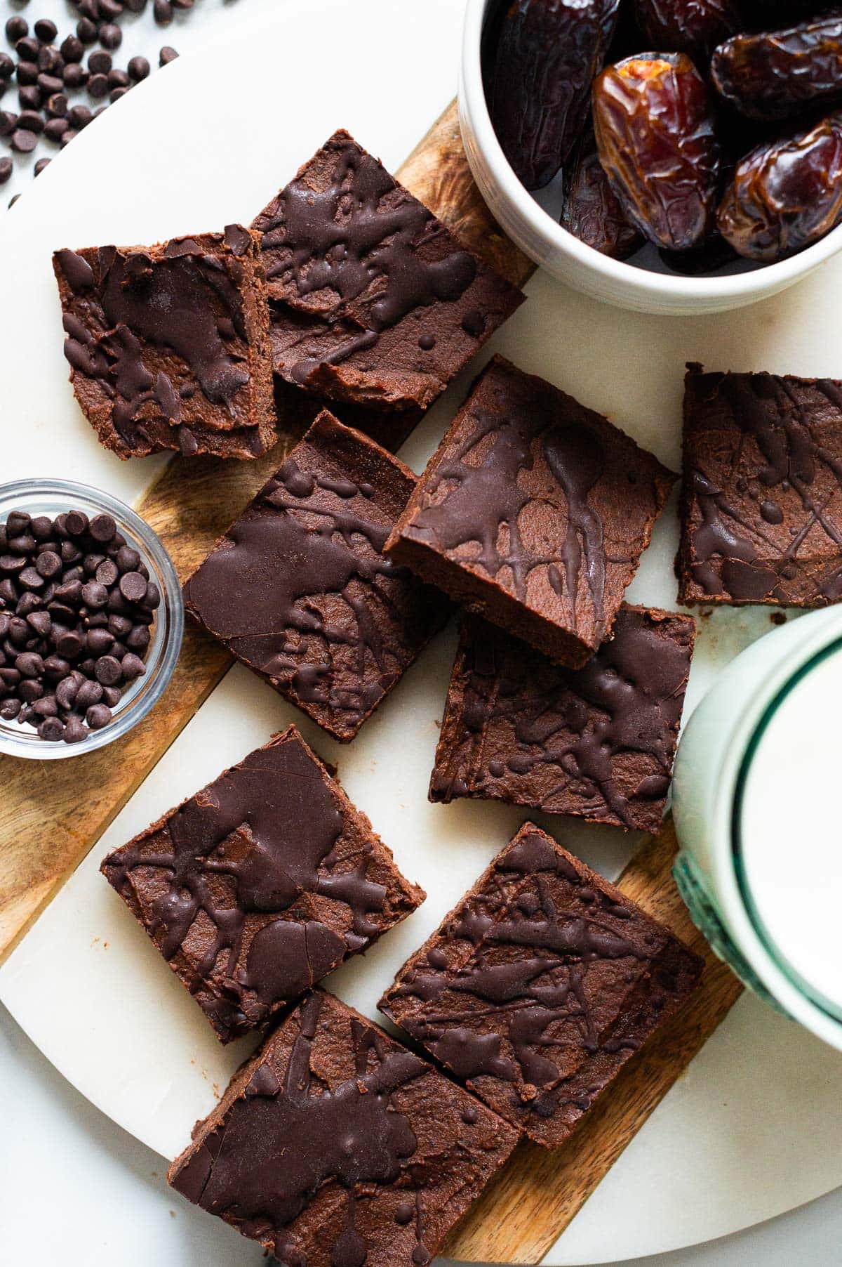 No bake brownies on a serving board. Milk in a glass, dates and chocolate chips in bowls.