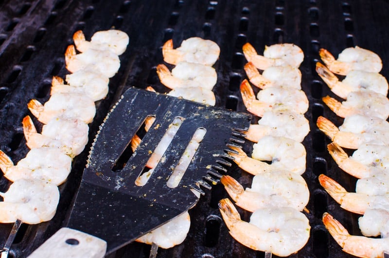 Pressing grilled shrimp skewer with metal spatula on the grill.