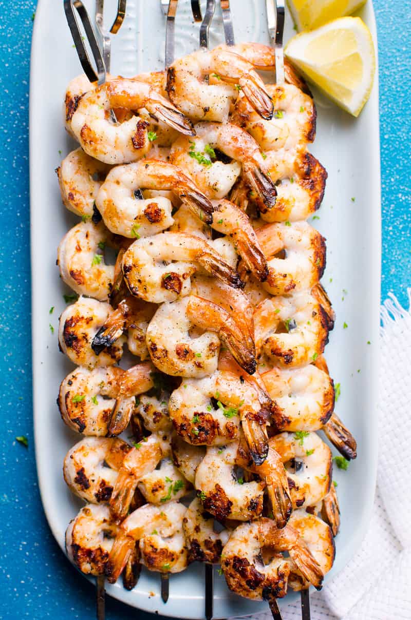 Grilled shrimp skewers served on a platter with a lemon wedge.