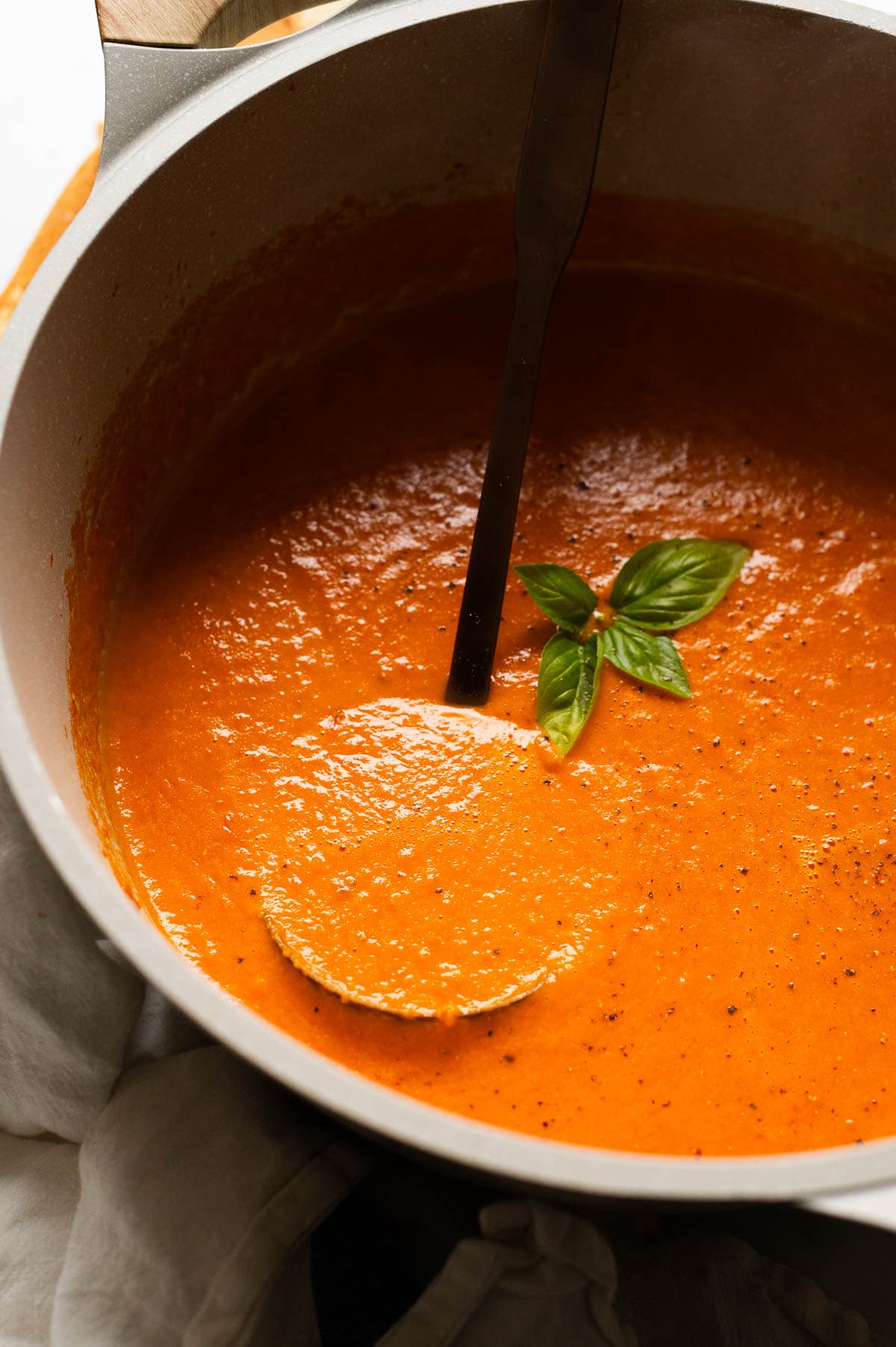 Tomato soup in a pot with ladle and garnished with basil.