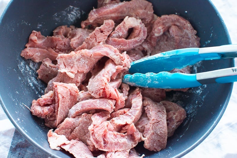 Raw steak in a bowl being mixed with cornstarch.