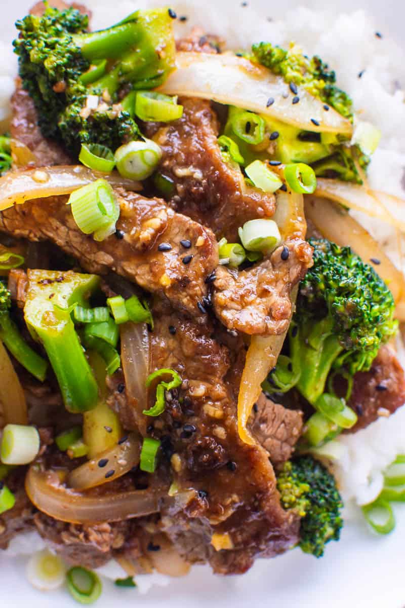 Beef and broccoli garnished with black sesame seeds over rice on plate. 