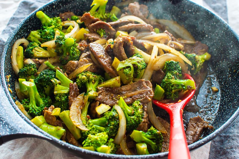Healthy Beef and Broccoli in black skillet with red spoon.