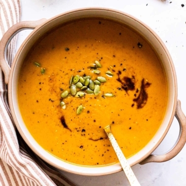Healthy pumpkin soup in a bowl with pumpkin seeds, soy sauce. Striped linen beside bowl.