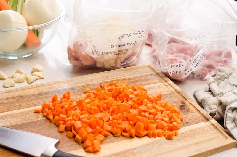 Chopped carrots on a cutting board, freezer meals in bags and vegetables in a bowl on a counter.