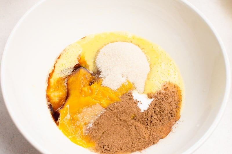 Egg, pumpkin puree, pumpkin pie spice, vanilla extract in white bowl.