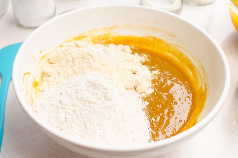Almond flour and oat flour being added to pumpkin puree ingredients in bowl.