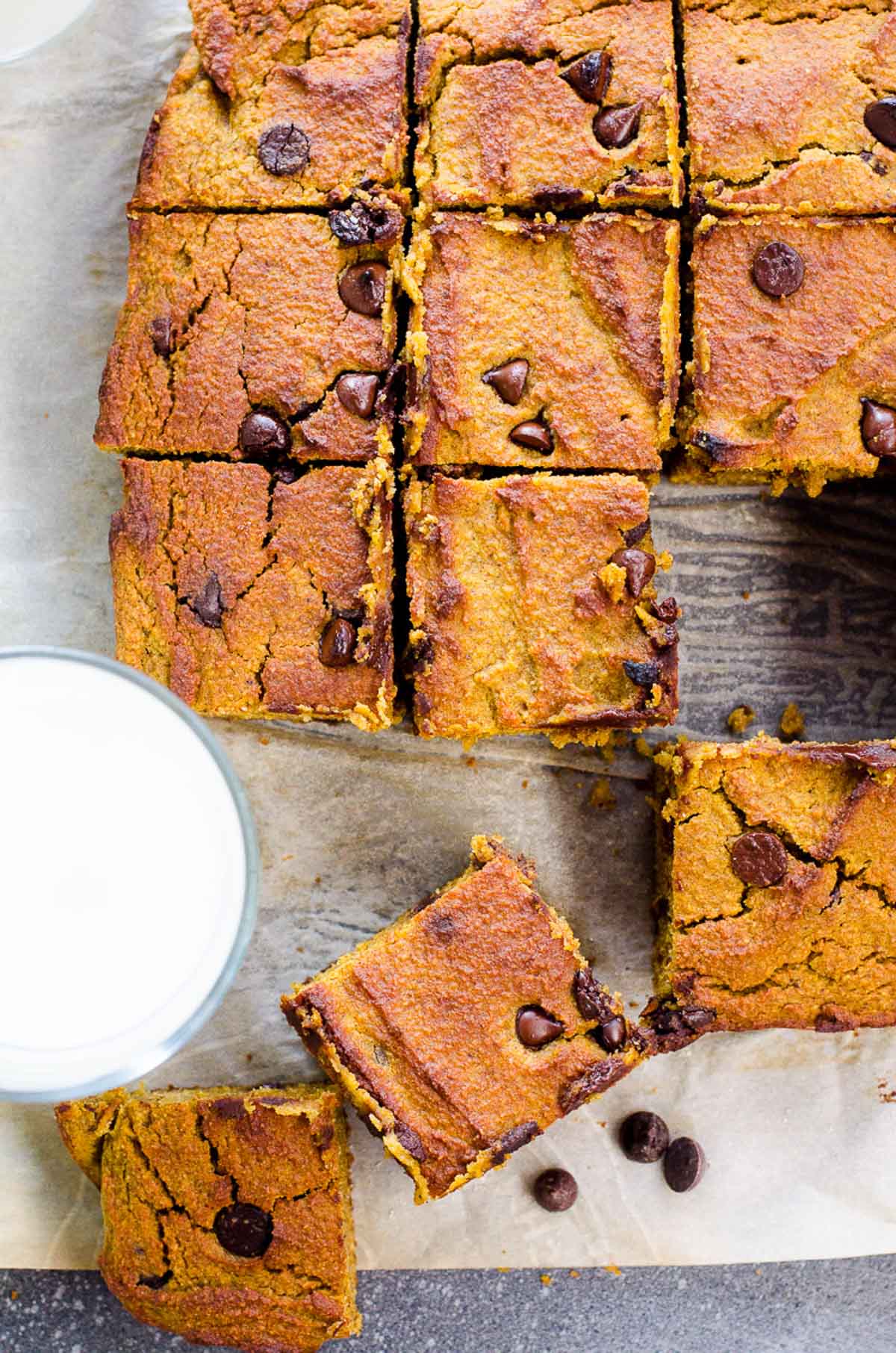 Healthy pumpkin bars cut into squares on parchment paper with a glass of milk.