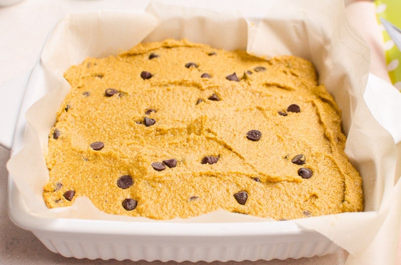 Unbaked pumpkin bars dough flattened in parchment lined pan.