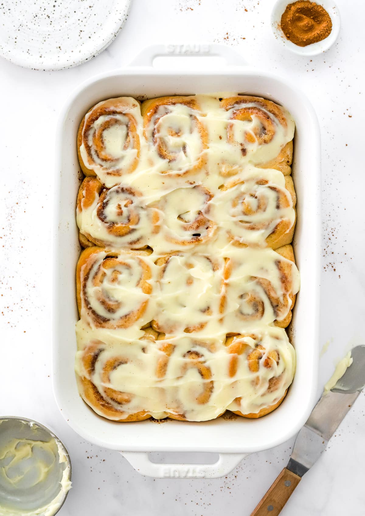 Twelve healthy cinnamon rolls with cream cheese frosting in white baking dish.