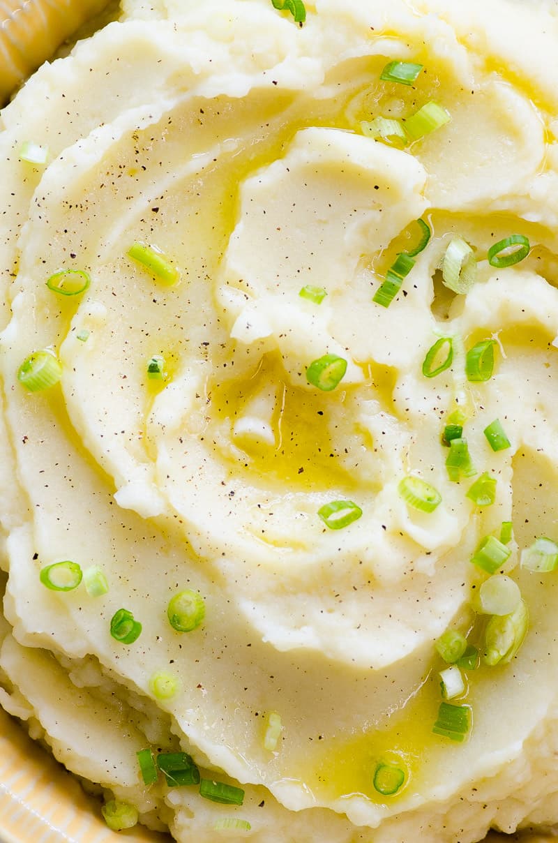 A closeup of healthy mashed potatoes with melted butter, pepper and green onion on top.