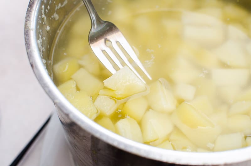 Fork poking cooked potato in a pot.