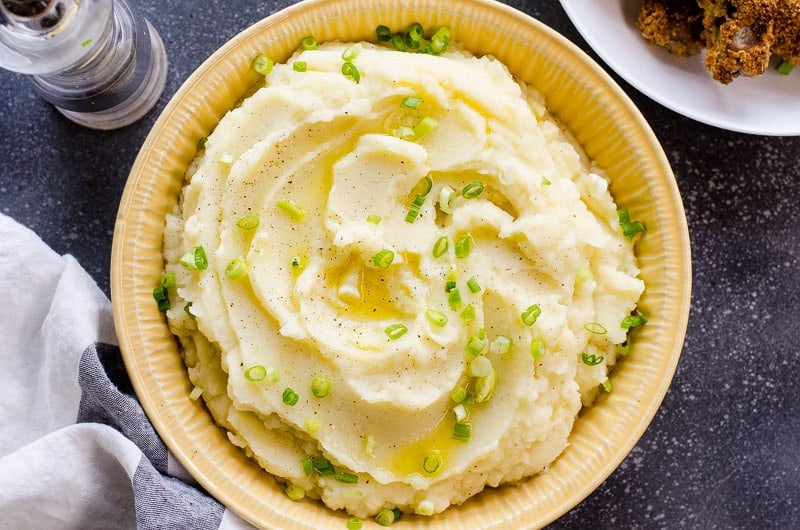 Homemade creamy mashed potatoes in a yellow dish garnished with green onion.