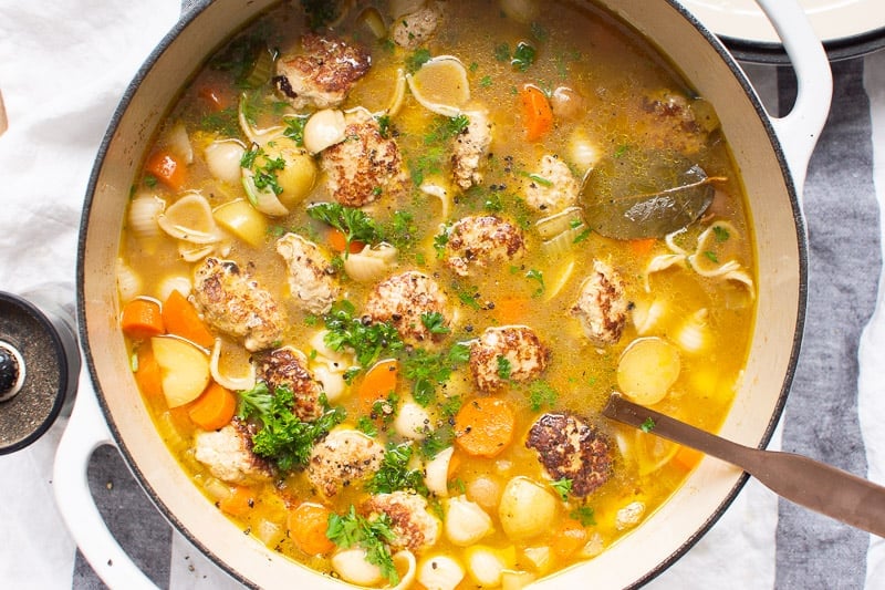Turkey meatball soup with vegetables and noodles garnished with fresh herbs and bay leaf in large pot.