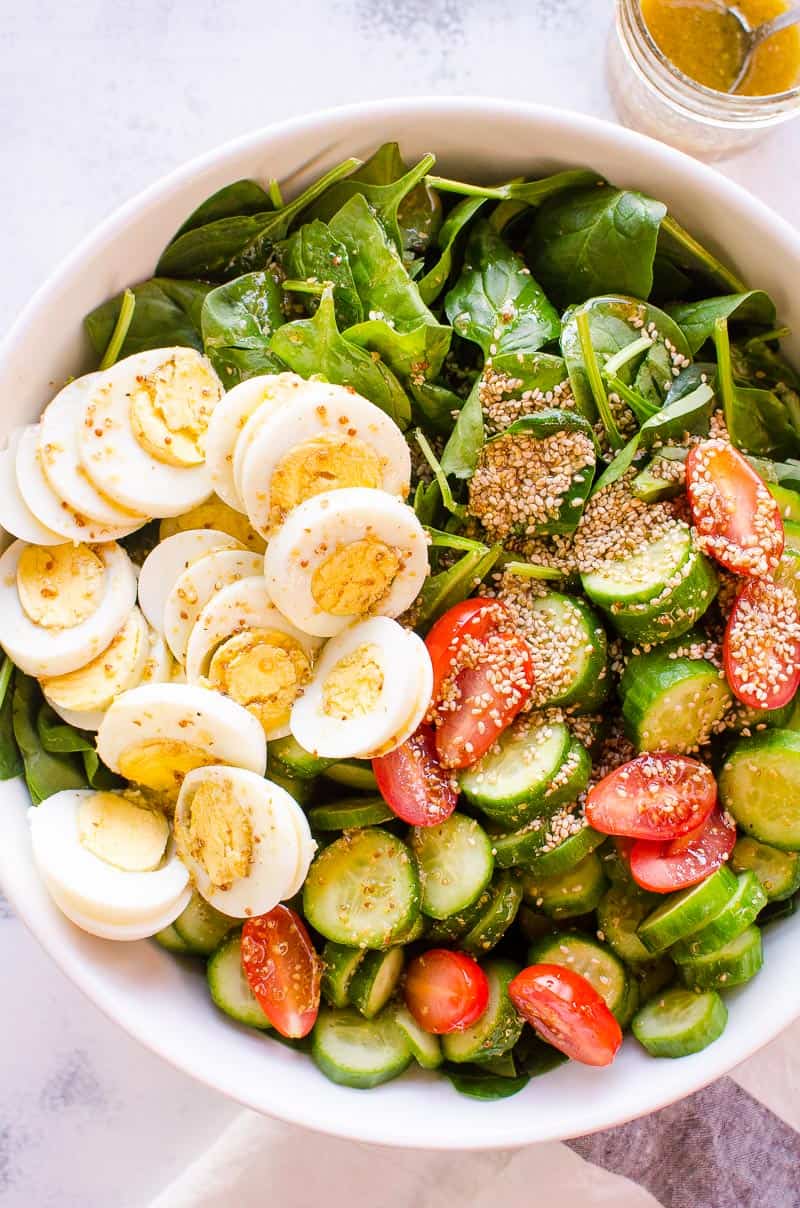 Healthy spinach salad with hard boiled eggs, cucumber and tomato. 