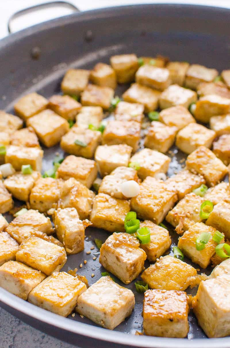 Crispy pan fried tofu garnished with sesame seeds and green onion in a skillet.