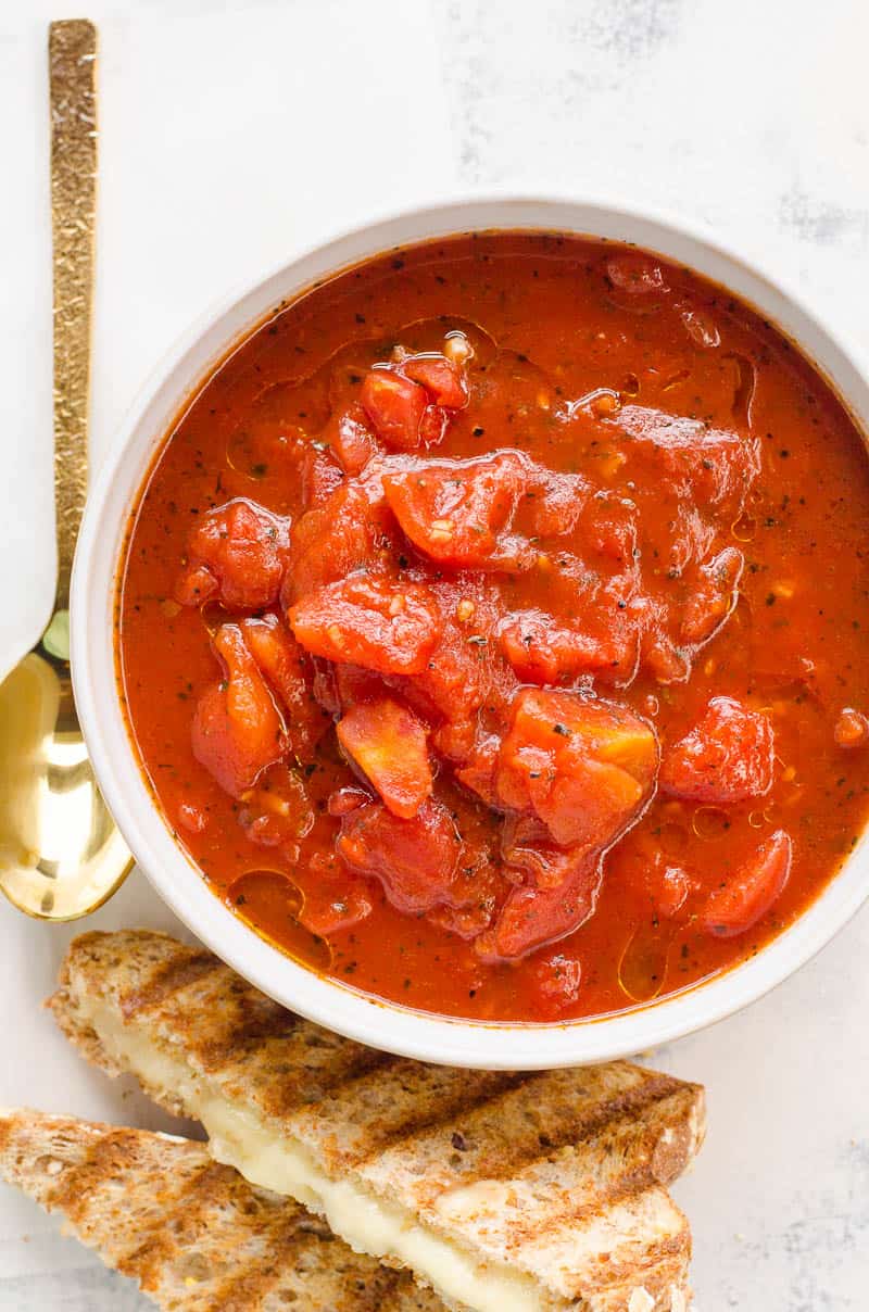 b\Bowl of healthy tomato soup beside grilled cheese sandwich and spoon.