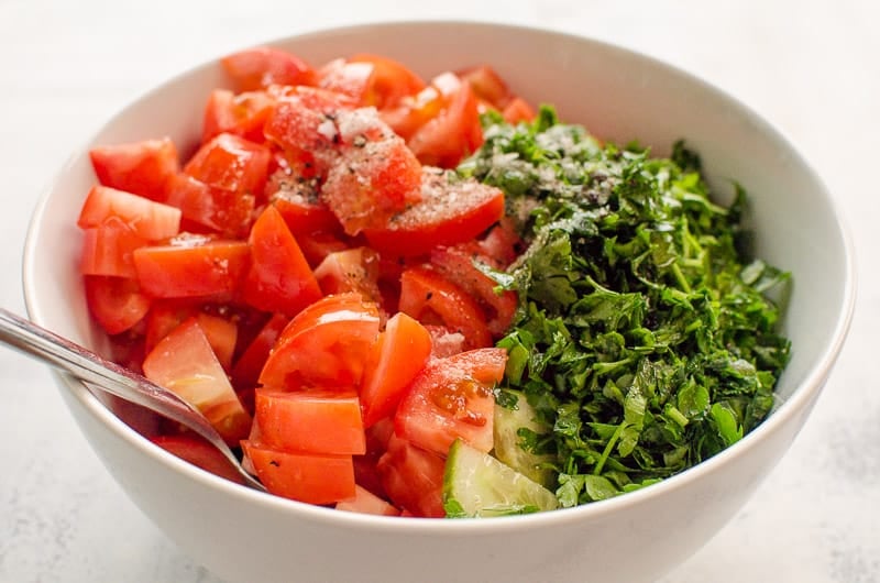 Chopped tomatoes, cucumber and cilantro in a white bowl with a fork.