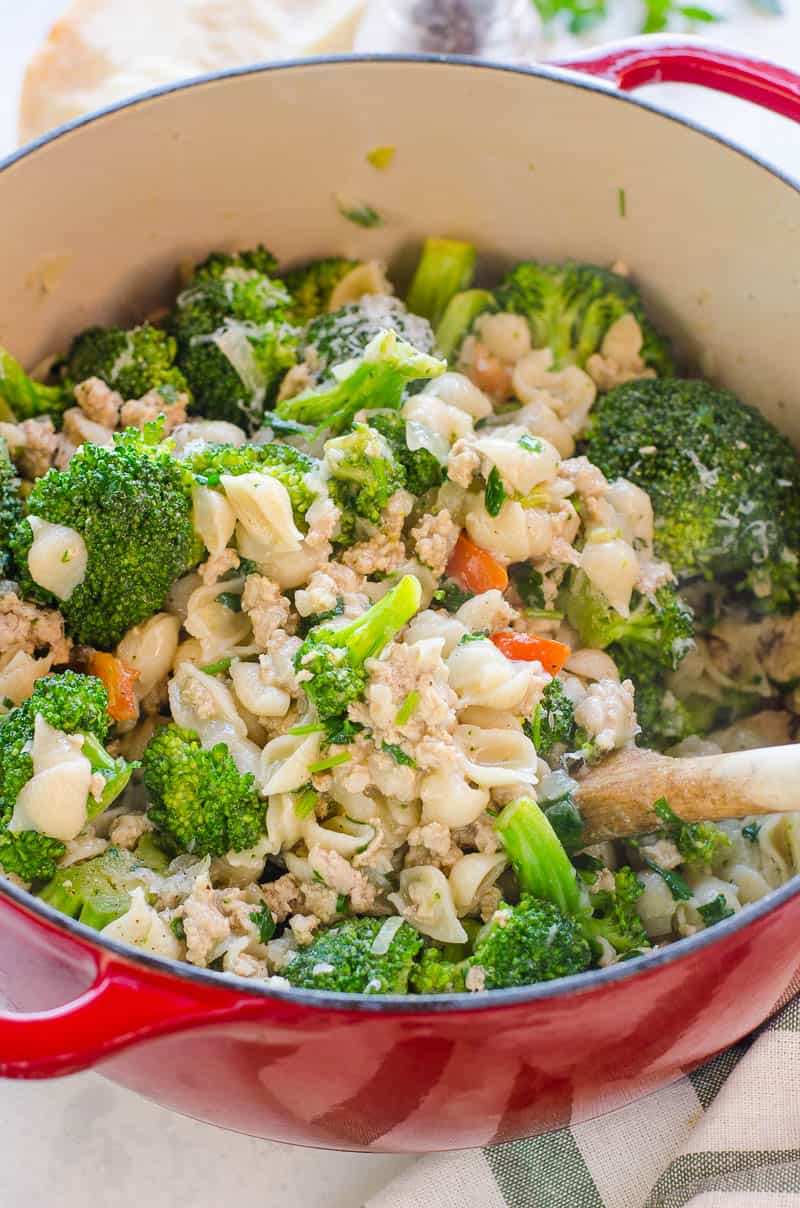 Ground turkey and broccoli pasta in a red pot with a wooden spoon.