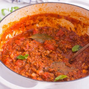 Homemade meat sauce in a white pot with basil.