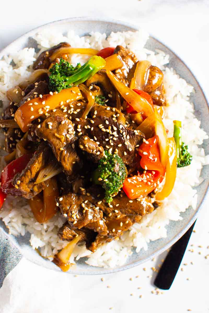 Beef stir fry recipe served over white rice and garnish with sesame seeds.