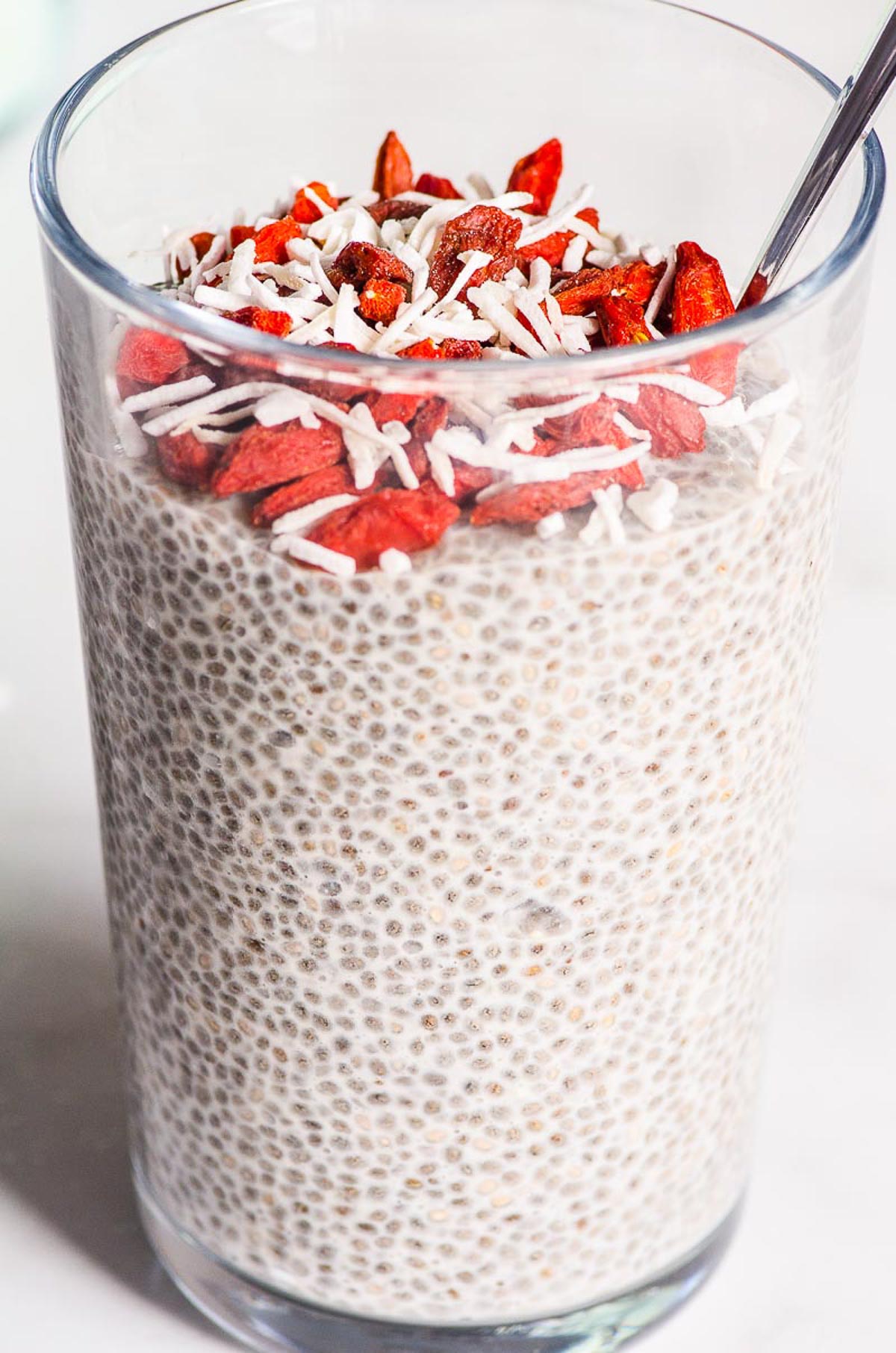 Vanilla chia pudding with goji berries and coconut flakes in a glass with a spoon.