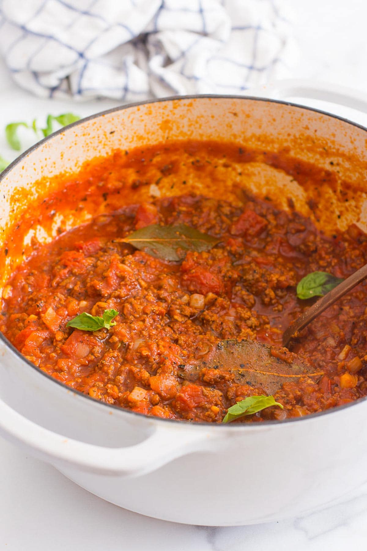 Homemade meat sauce in white pot with bay leaves and fresh basil.