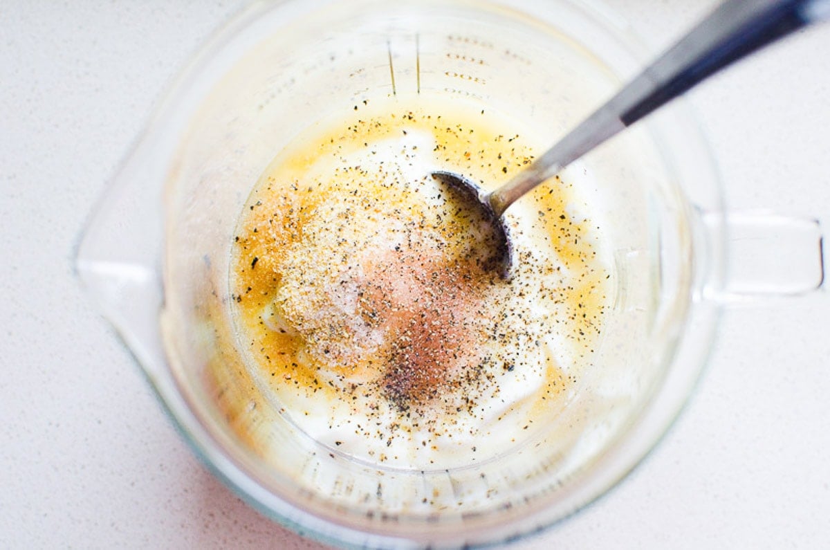 Yogurt, vinegar, garlic powder, salt and pepper in measuring cup with a fork.