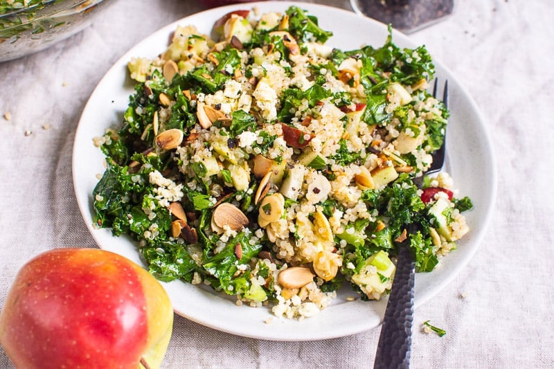 Kale apple walnut salad with quinoa on white plate with black fork