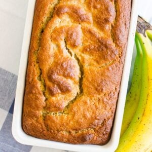 Almond flour banana bread in white loaf pan and bananas nearby.