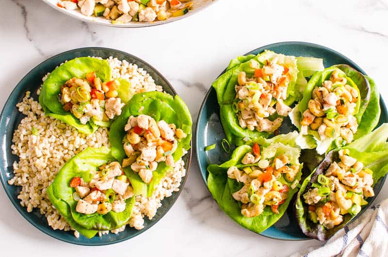 Healthy chicken lettuce wraps served on plates. One plate of lettuce wraps served over brown rice. 