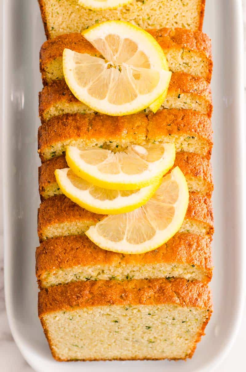 Healthy lemon zucchini bread sliced on a plate with sliced lemons on top.