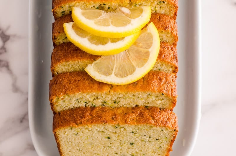 healthy lemon zucchini bread sliced on a white plate garnished with slices of lemon